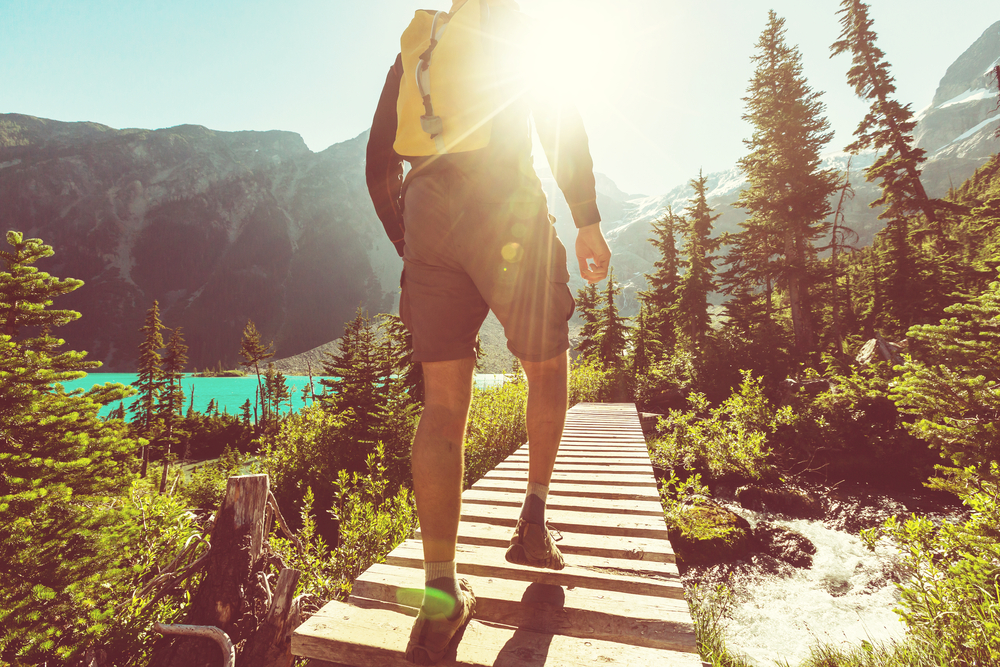 Man Hiking Over a Wooden Bridge in the Mountains With the Sun Shining