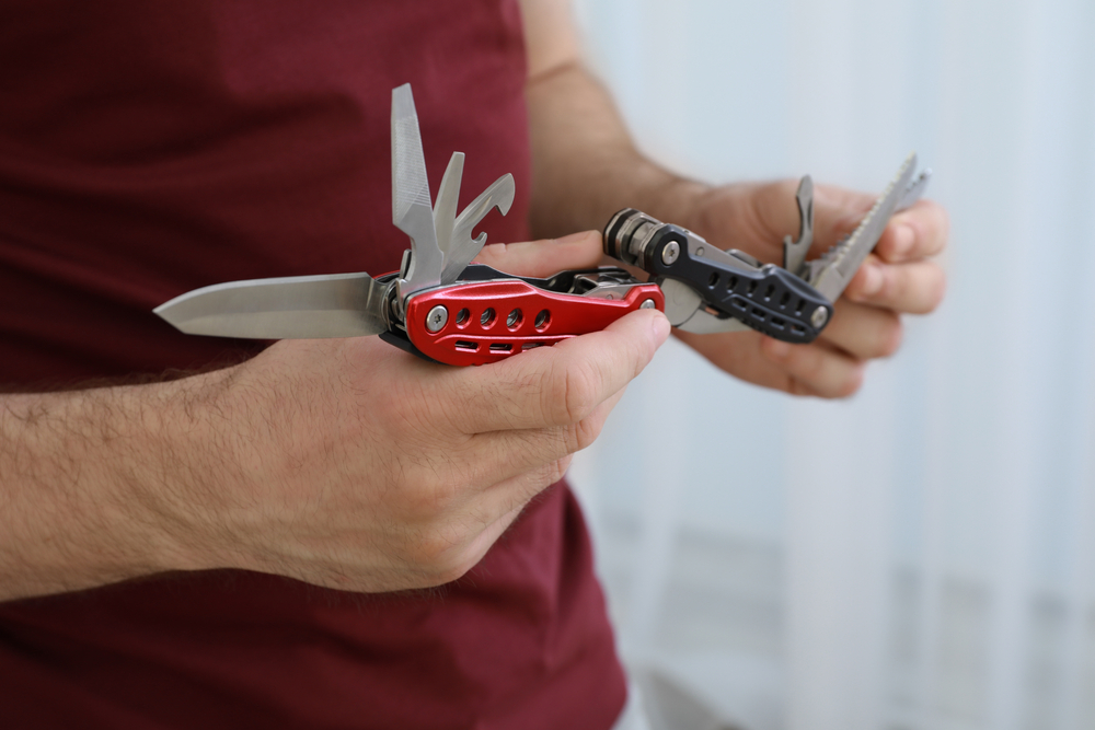 Man holding black and red multi-tools with blades extended